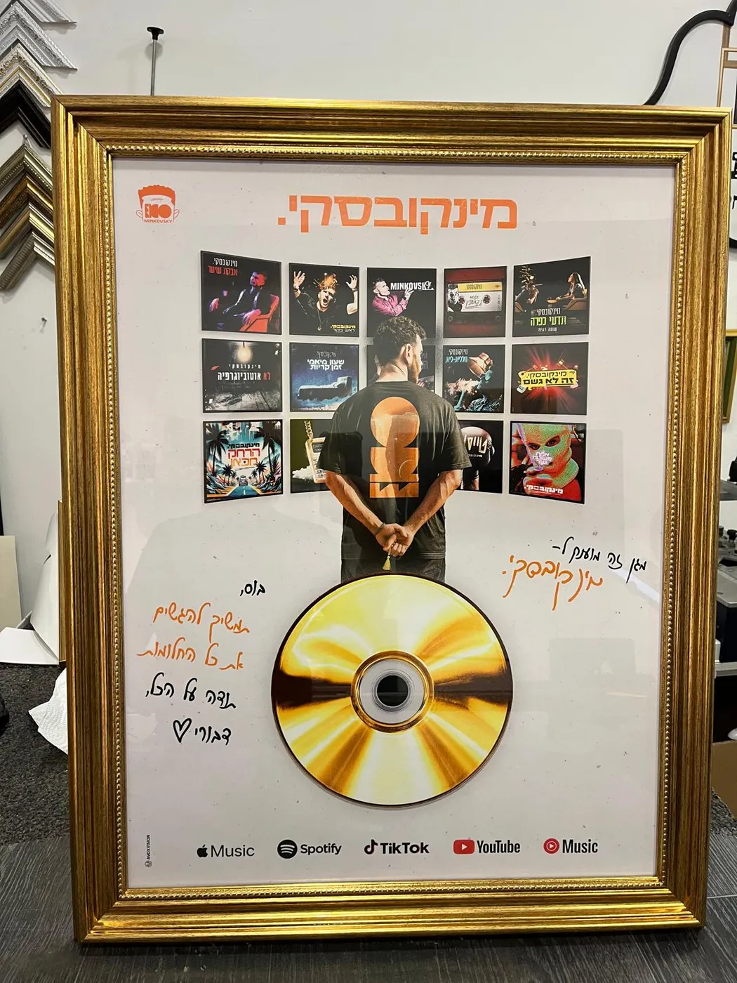 מסגור פרס דיסק זהב — CD מוזהב מקובע מעל הדפס עם הקדשות בכתב יד, במסגרת זהב מעוטרת